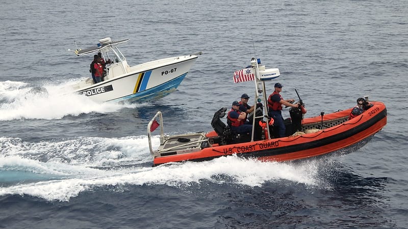 A patrol vessel with law enforcement markings idles alongside a small motorboat on open water.