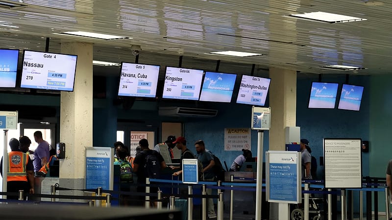 Passengers with hand luggage walk through a glass connecting corridor between airport terminals.