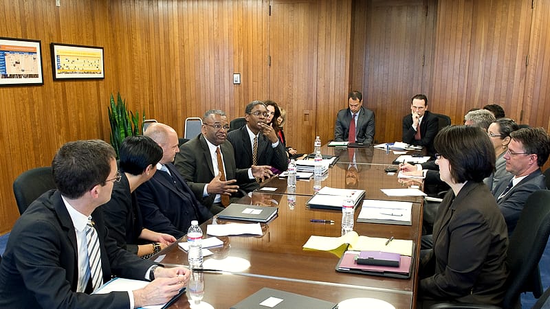 Officials seated across a conference table sign and exchange documents during a formal meeting in a government building.