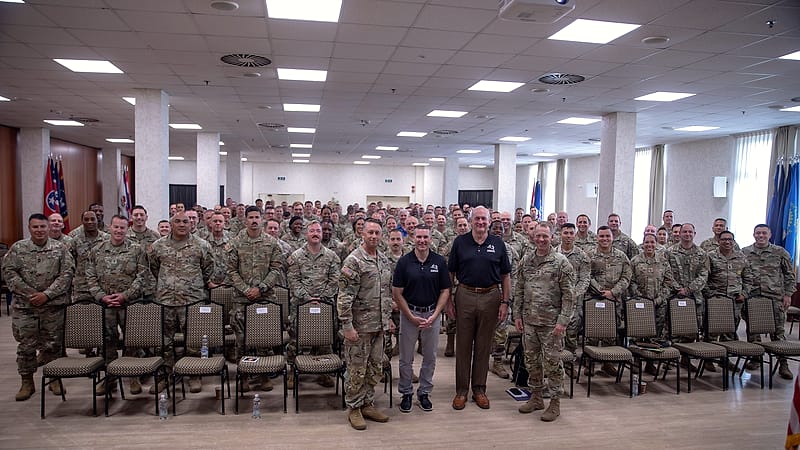 Uniformed attendees sit in rows at a professional development seminar facing a speaker at the front of the room.