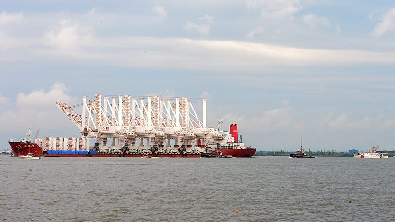 Container ship crew in overalls descend a gangway onto a quayside beside stacked containers.