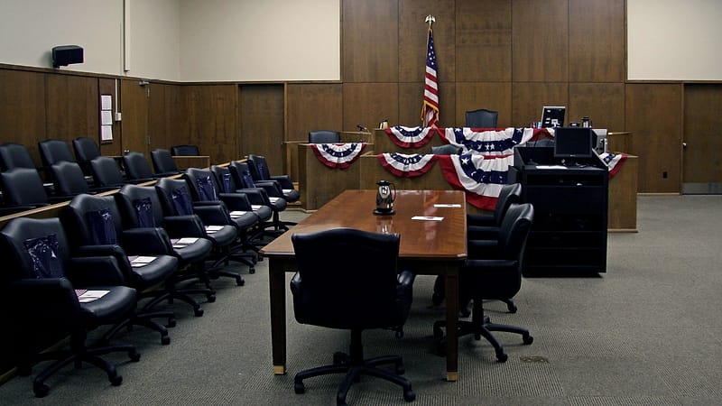 A federal courthouse corridor with tall doors and a row of empty wooden benches along the wall.