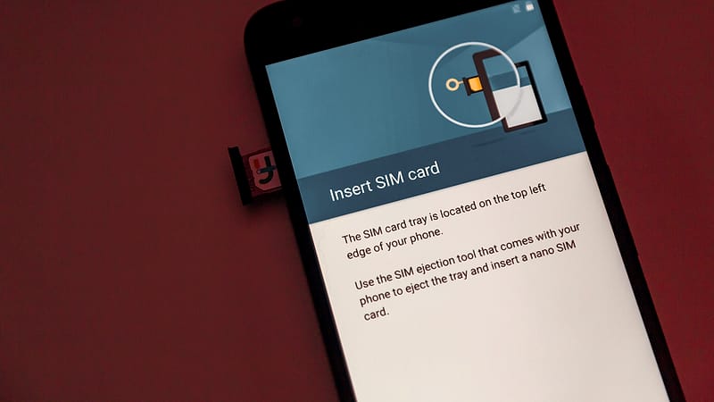 A person holding two mobile phones side by side with a SIM card tray open on one of them.