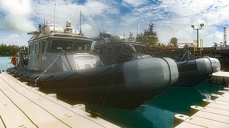 Sailboats and motor cruisers lie in adjacent slips at a marina with power pedestals and finger docks between them.