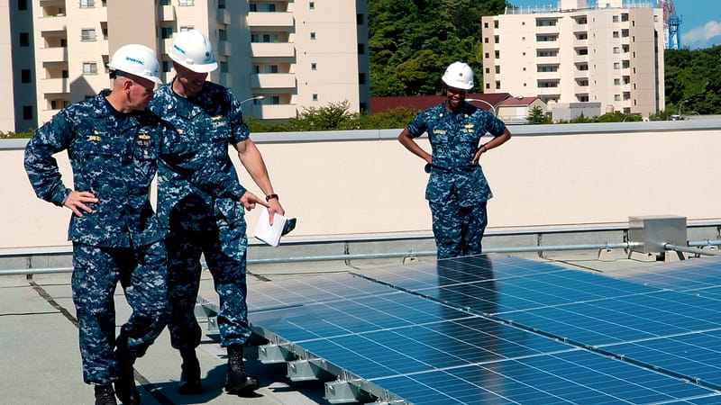 Solar panels mounted on a residential roof with an electric meter and conduit running down the exterior wall.