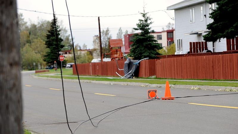 A line crew working from an aerial bucket on a damaged power pole with broken conductor hanging beside it.