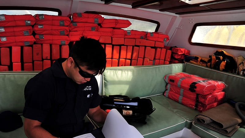 Orange life jackets, a fire extinguisher and a handheld horn arranged on a boat deck during an equipment check.