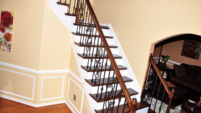 A worker applies finishing trim inside a nearly complete room, with tools and offcuts on the floor nearby.