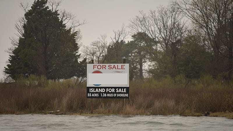 A for-sale sign stands on the front lawn of a suburban house with a converted garage frontage behind it.
