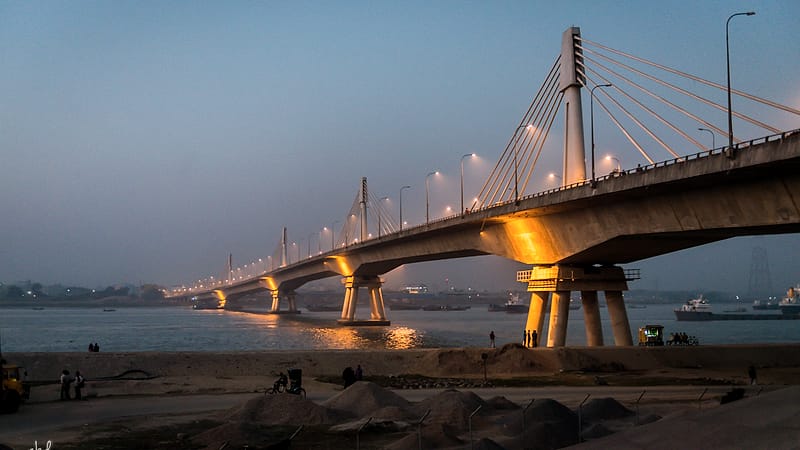 A long road bridge photographed from the bank, carrying traffic across a wide river toward a distant city.