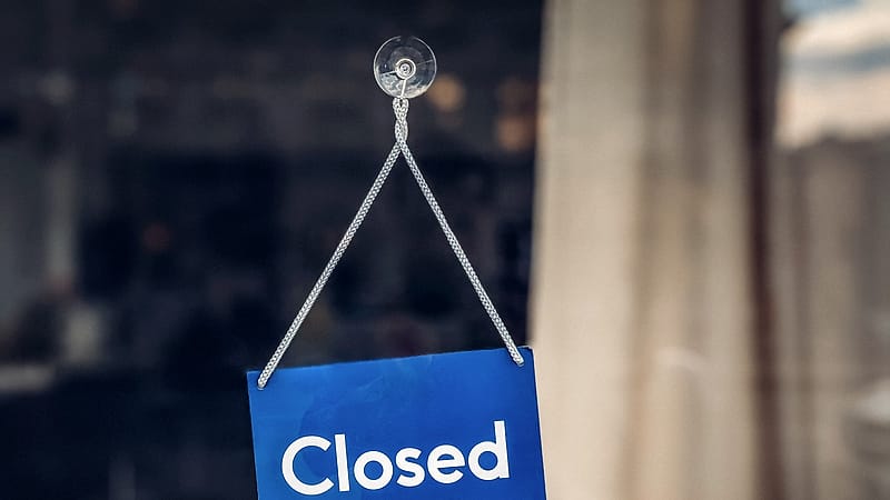 A closed sign hangs against the glass of a shop door with the interior dark behind it.
